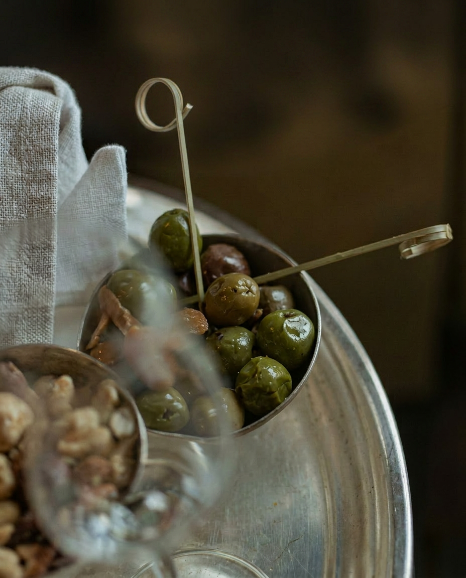Green olives in a small silver bowl on a rustic table